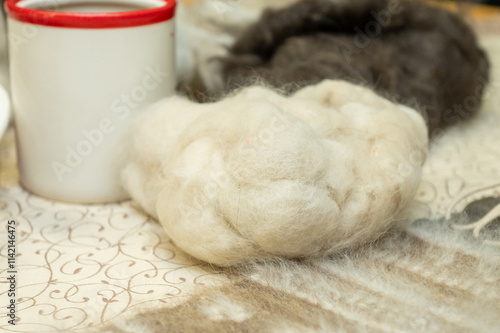 Soft wool fibers and red-rimmed mug on ornate tablecloth photo