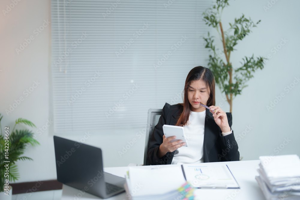 Asian businesswoman holding pen and using calculator while working on laptop computer with business document on desk at modern office, thinking expression Asian businesswoman holding pen and using calculator while working on laptop computer with business document on desk at modern office, thinking expression
