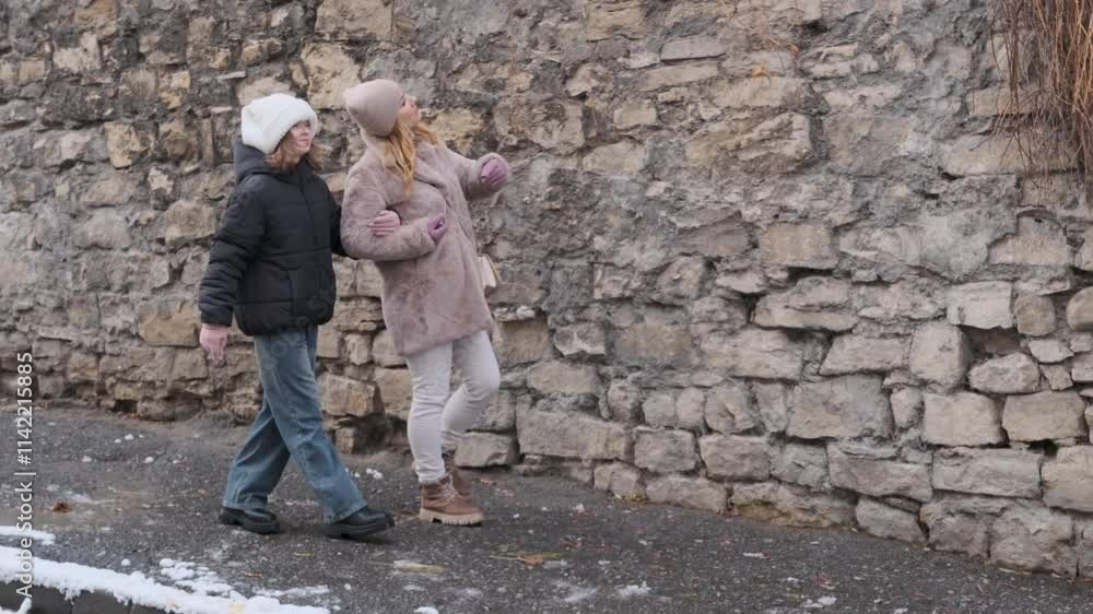 Woman is pointing and showing something to her daughter while they are walking along a stone wall in slow motion Woman is pointing and showing something to her daughter while they are walking along a stone wall in slow motion