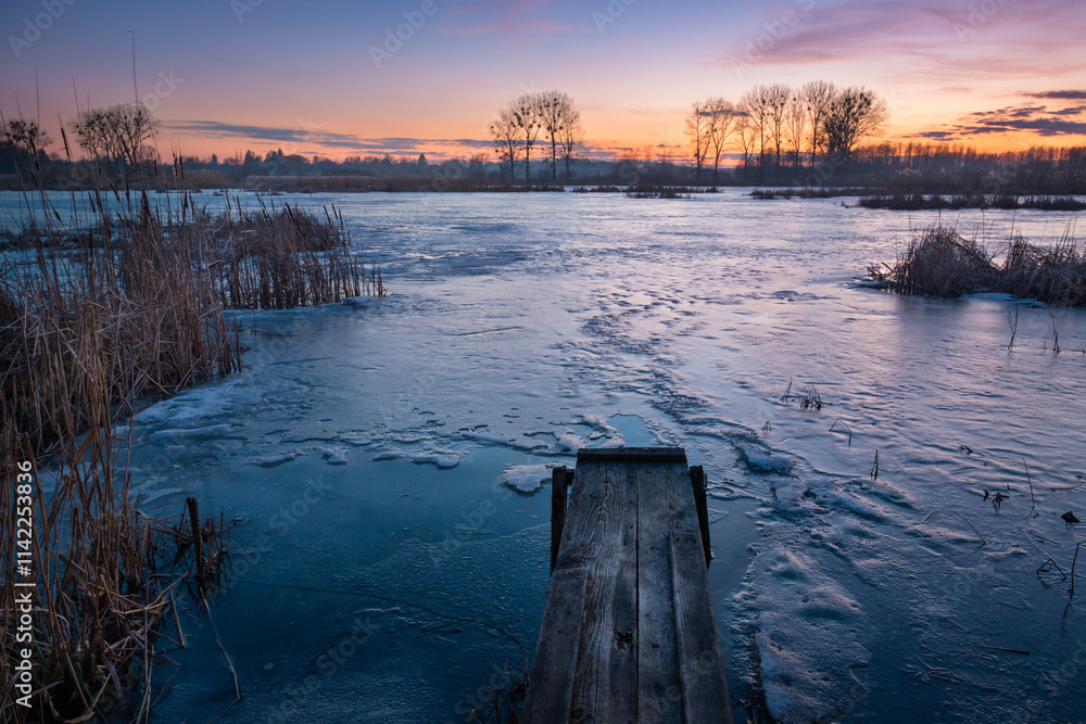 Fototapeta premium A small wooden bridge in front of a frozen lake during sunset, Stankow, Lubelskie, Poland