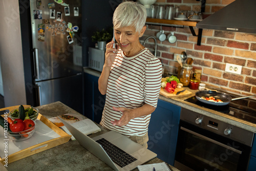 Senior woman cooking in kitchen while talking on phone photo