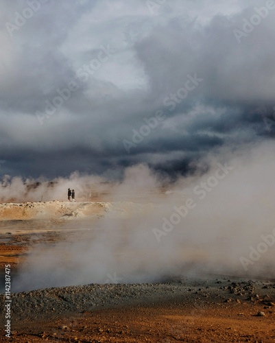 People in steaming geothermal landscape under dramatic cloudy skies in Iceland