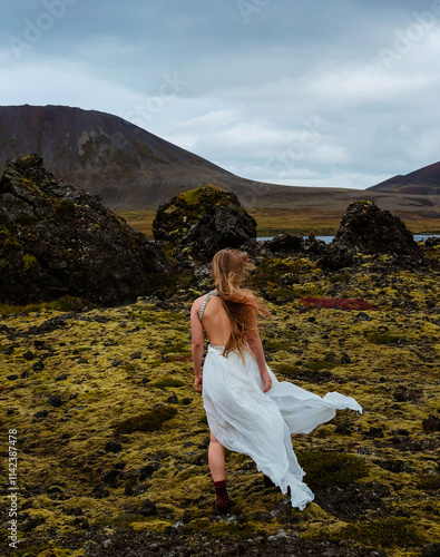 Ethereal beauty in flowing white dress amidst Icelandic moss plains.