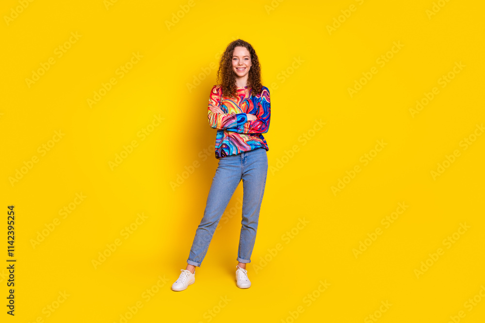 Joyful young woman with red curly hair in colorful sweater standing confidently against vibrant yellow background Joyful young woman with red curly hair in colorful sweater standing confidently against vibrant yellow background