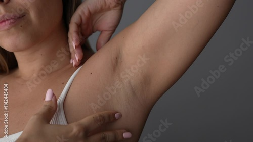 Young blonde woman stroking the armpit showing her clean smooth skin after depilation on a dark grey background. The result of laser hair removal. Slow motion