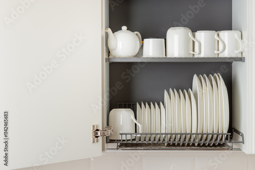 A dish-drying rack integrated into a wall cabinet in a modern kitchen with white ceramic kitchenware, plates and mugs, arranged orderly