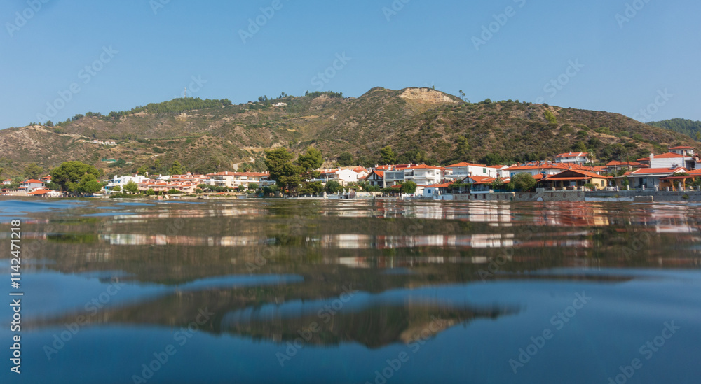 A serene village lies on the coast, under a wide bright sky with a combination of greenery and classic Mediterranean architecture along the shore. A serene village lies on the coast, under a wide bright sky with a combination of greenery and classic Mediterranean architecture along the shore.