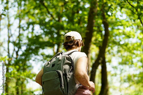 Elderly woman with backpack hiking in forest. Back view. Copy space.