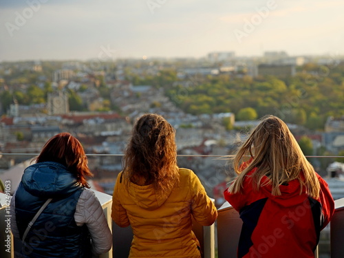 Girls tak a panorama photo of the ancient city with a smartphone. An observation deck at the town hall of the central Rinok square of the city of Lviv in Ukraine. Tourist selfie place on sunset photo