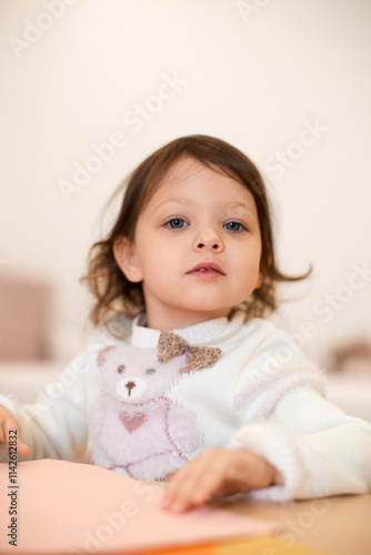 little child girl holding multi-color paper while sitting by table at home