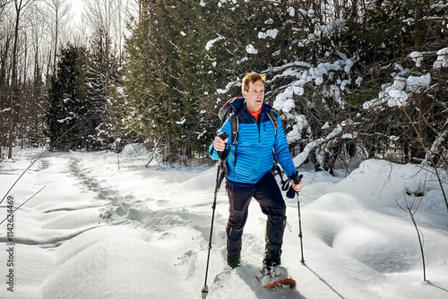 A man in blue outdoor active apparel and backpack, snowshoeing off trail through deep powder snow, in the woods on an untracked trail. photo