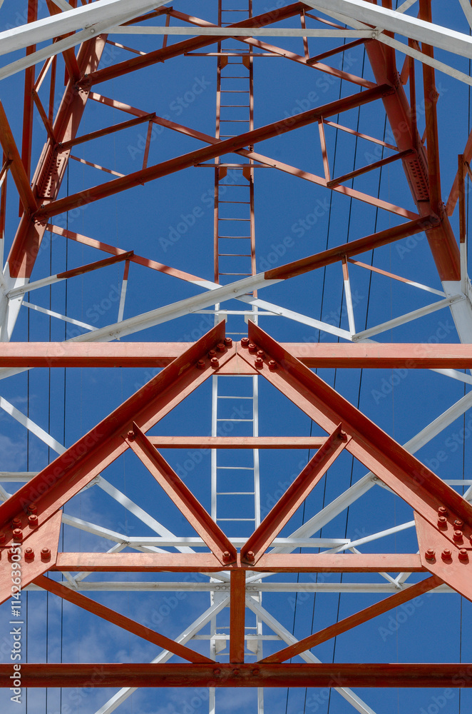 Low angle view of a large transmission tower with a distinctive geometric design, featuring red and white colors Low angle view of a large transmission tower with a distinctive geometric design, featuring red and white colors