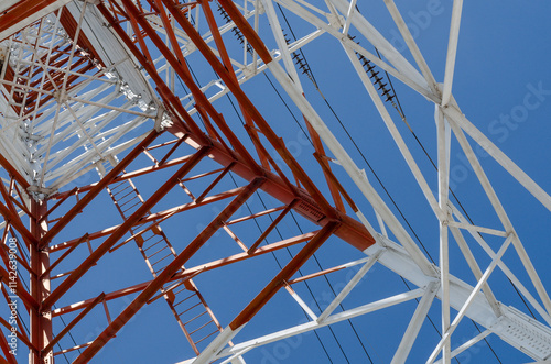 Low angle view of a large transmission tower with a distinctive geometric design, featuring red and white colors