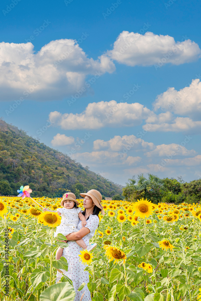 Fototapeta premium Mother carries daughter in sunflower field,Carefree mother and daughter spending leisure time in sunflower field
