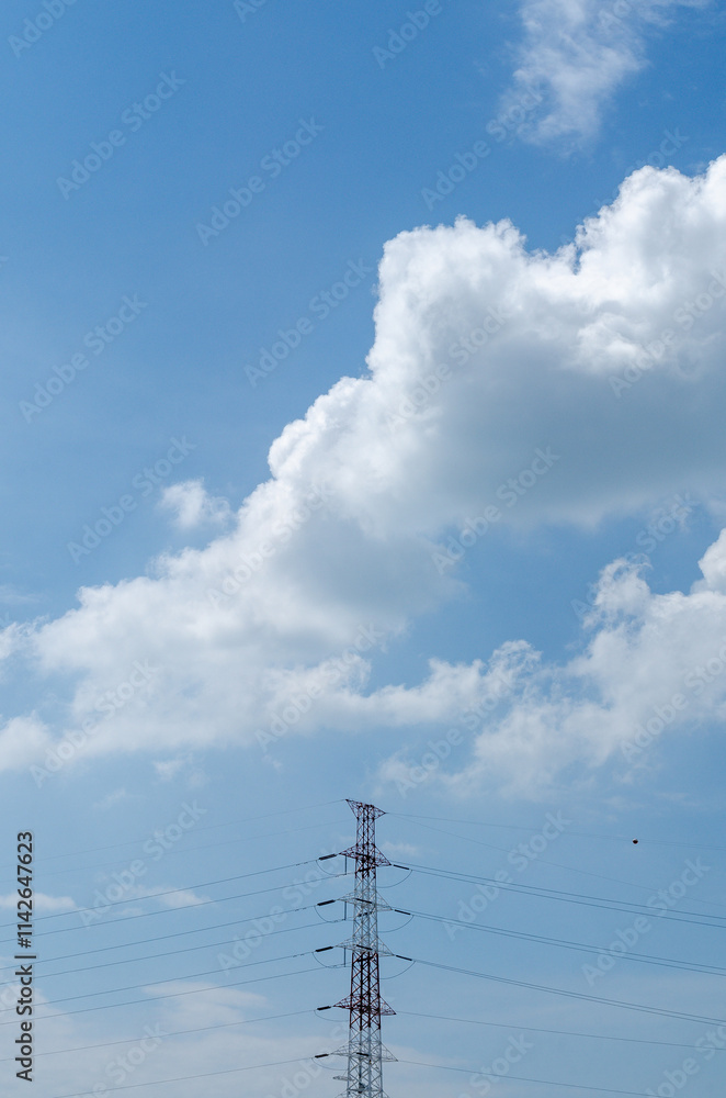 A tall electrical power line tower rising against a blue sky filled with fluffy white clouds A tall electrical power line tower rising against a blue sky filled with fluffy white clouds