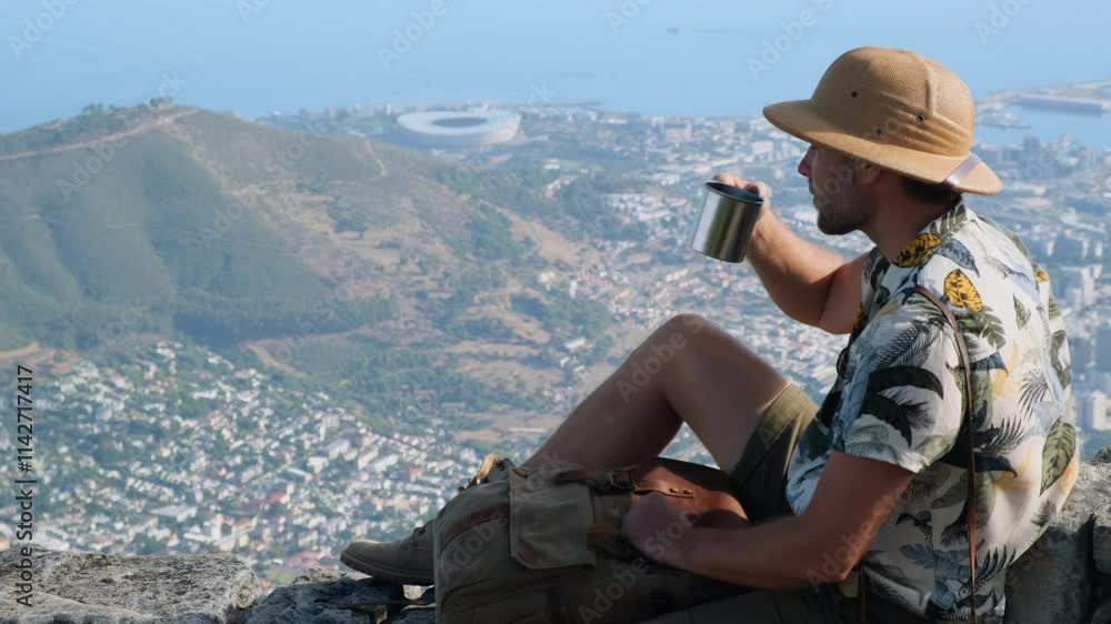 man hiker in boots drinking a hot drink from a mug sitting on a mountain peak relaxing after hiking and taking a break. A hiker wearing a sun hat and sunglasses, looking out over a scenic vista man hiker in boots drinking a hot drink from a mug sitting on a mountain peak relaxing after hiking and taking a break. A hiker wearing a sun hat and sunglasses, looking out over a scenic vista