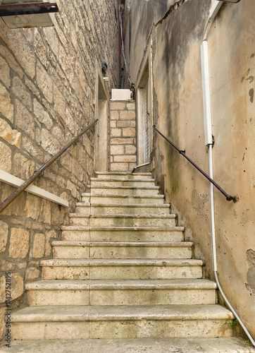 Korcula, Croatia - June 30, 2024: Steps leading higher while becoming narrower as a triangle is created by two house walls on Prolaz Tri Sulara square photo