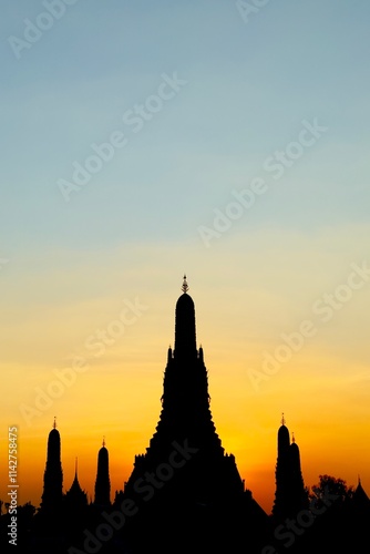 Wat Arun Ratchawararam in Bangkok, Thailand, with a bright golden orange sunset as the backdrop. The reflection of the temple on the water below creates a peaceful and elegant atmosphere.