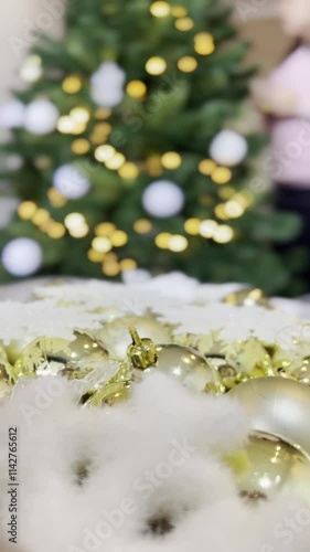 A person is putting gold and white Christmas ornaments on a table