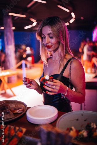 A woman is selecting food at a banquet. She moves along a beautifully arranged buffet table, carefully choosing dishes photo