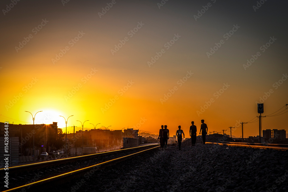 silhouette of unrecognizable young men walking between railroad lines in a suburban area at sunset time. silhouette of unrecognizable young men walking between railroad lines in a suburban area at sunset time.