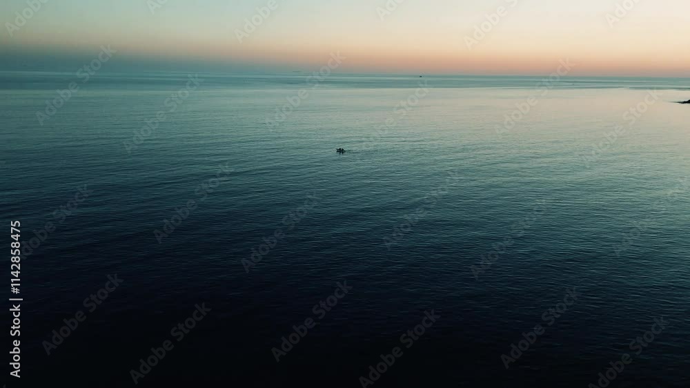 Golden light illuminating serene sky above calm mediterranean waters, small fishing vessel drifting near rocky mersin coastline during sunset glow