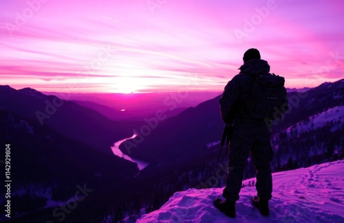 Soldier stands on snowy mountain peak at purple sunset. Majestic landscape with river winding through valley. Dramatic colours. Peaceful scene. Military man observes nature. photo