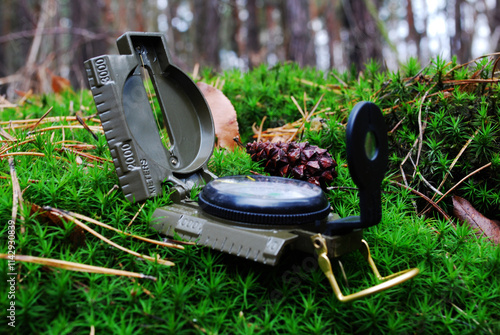 opened military compass on green moss in a wet forest