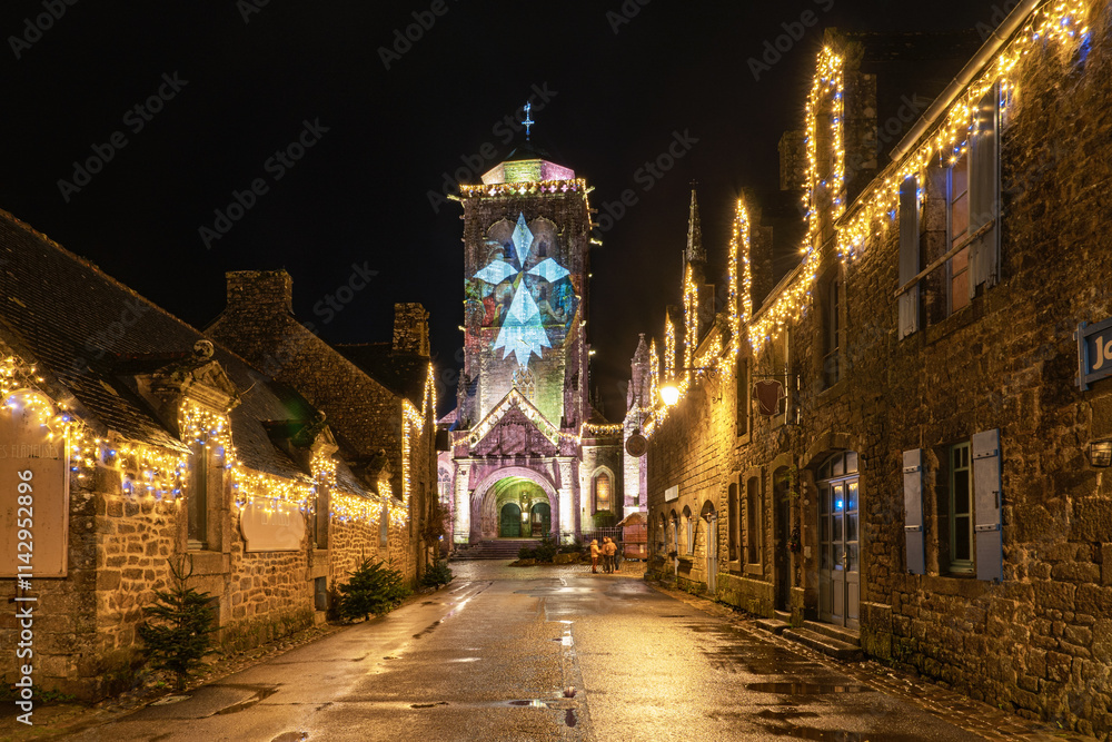 Fototapeta premium Le cœur de Locronan brille sous ses illuminations de Noël. Ses maisons de pierre et son église gothique sont magnifiées par une lumière douce et chaleureuse.