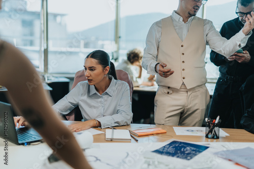 A group of business people engaged in a busy office setting. The team is collaborating on projects, working on laptops, and discussing ideas. The atmosphere is productive and goal-oriented. photo