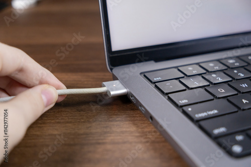 MagSafe charging cable connection to a laptop with LED light indicator glowing on a wooden desk surface photo