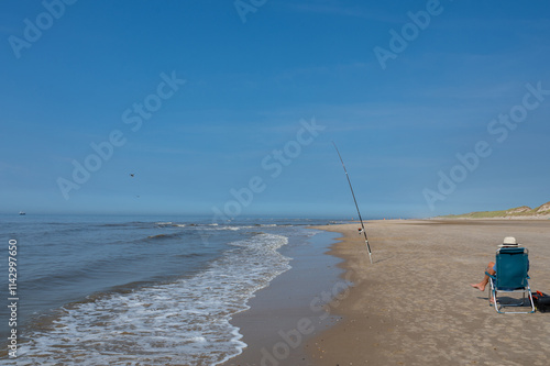 A fisherman sits on the beach with his fishing rod by the sea photo