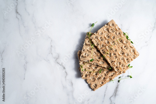 Pieces of crispbread with sesame seeds sitting on a marble background, whole-grain snacks. photo