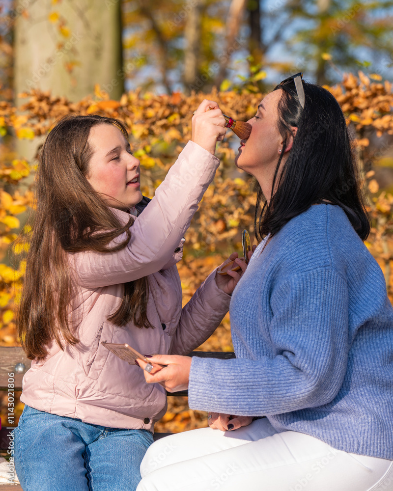 Fototapeta premium Mother and cute preschool daughter have fun together in nature in fall park, paint lips with lipstick, do each other's makeup, have nice time at home.Happy family.