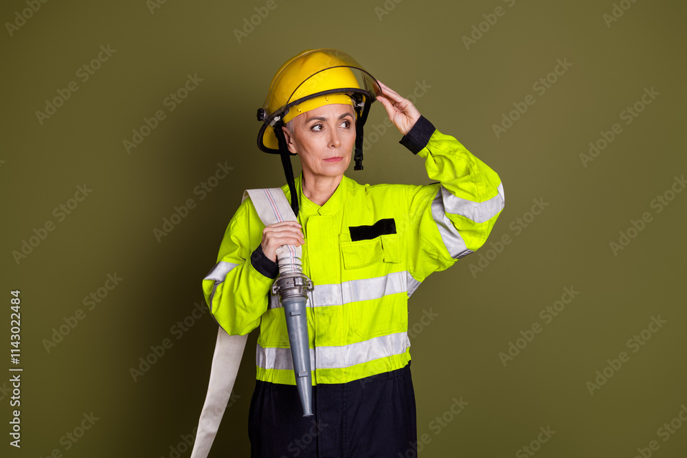 Mature female firefighter wearing protective gear with helmet and uniform against khaki background, ready for emergency response Mature female firefighter wearing protective gear with helmet and uniform against khaki background, ready for emergency response