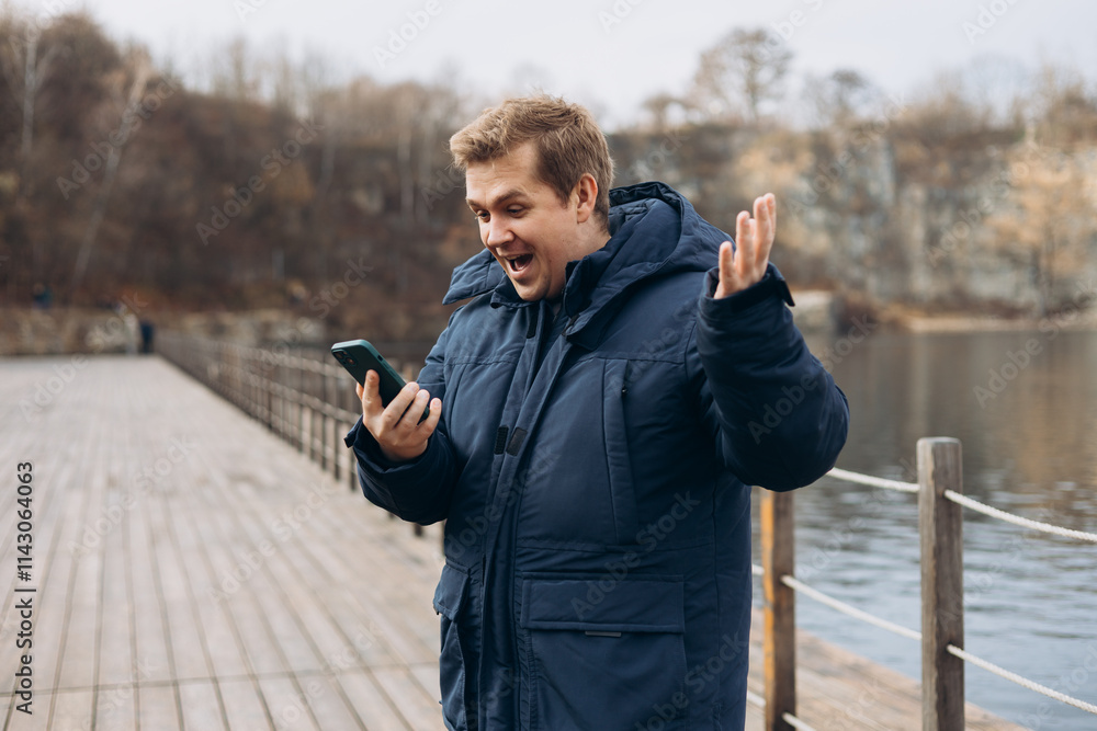 Male standing on the lake wooden pier. Happy man using phone, walking near river. Phone Communication. Happy won the game, lottery. Human emotions, facial expression concept