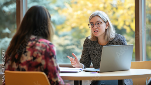 University professor guiding graduate student, reviewing materials together on round table with shared laptop during consultation photo