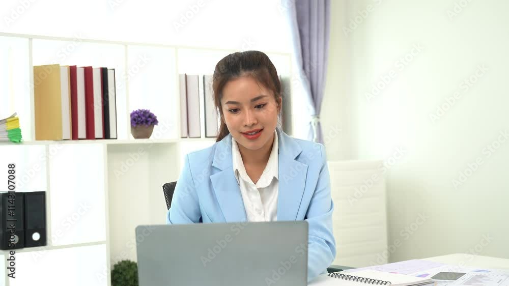 Focused and Confident: A professional woman in a blue blazer confidently works on her laptop in a modern office setting. Her determination and focus are evident as she navigates her tasks with ease. Focused and Confident: A professional woman in a blue blazer confidently works on her laptop in a modern office setting. Her determination and focus are evident as she navigates her tasks with ease.