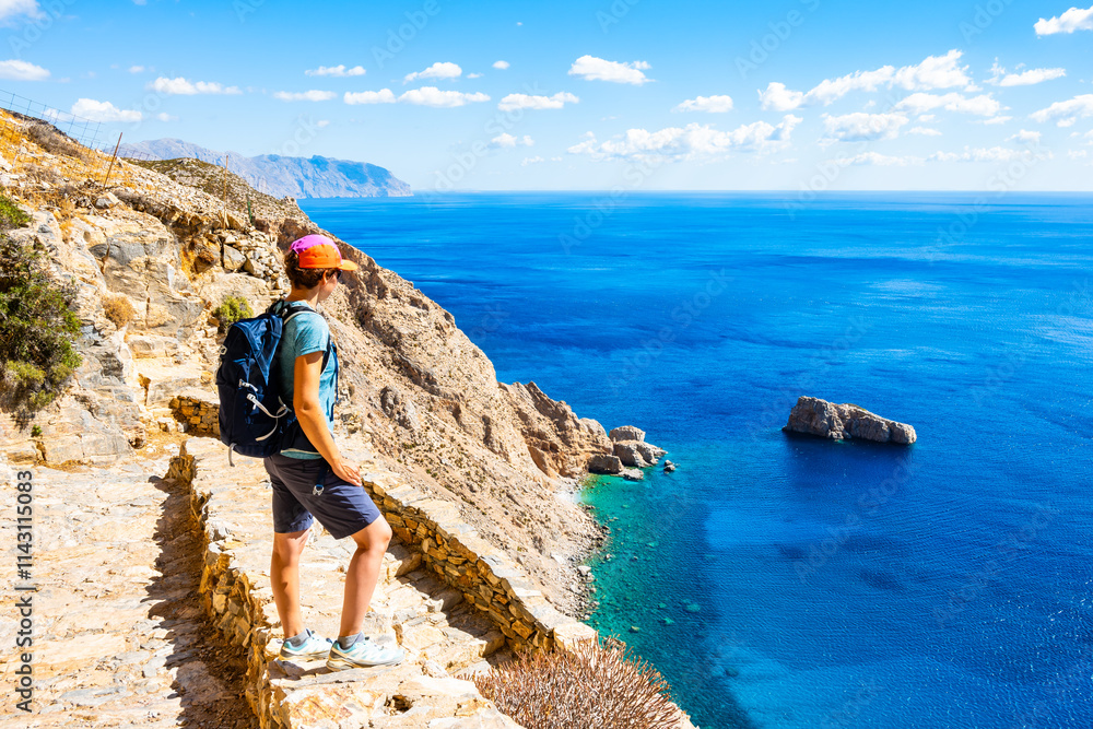 Woman tourist with backpack trekking to Panagia Hozoviotissa monastery and looking at sea coast, Amorgos island, Cyclades, Greece