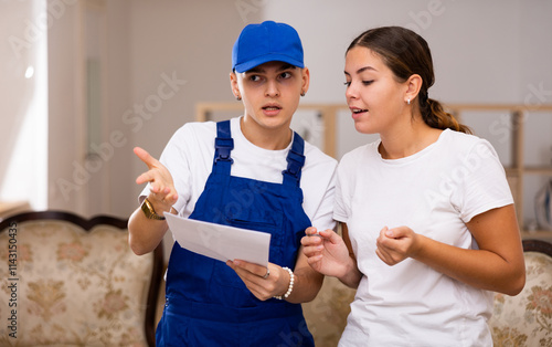 Master in uniform with documents in his hands discusses with the young landlady of the apartment the plan of repair work, making important notes on paper photo