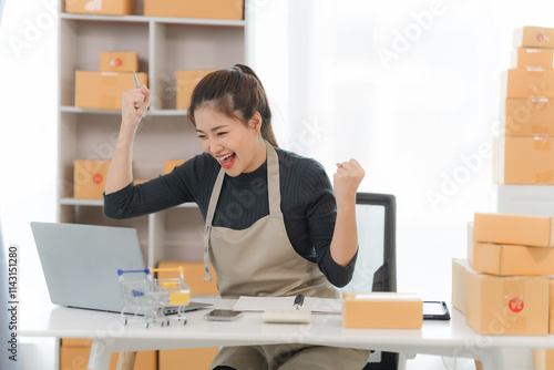 Online Business Success: Happy entrepreneur celebrating a successful online sale, surrounded by packages and using a laptop.   photo