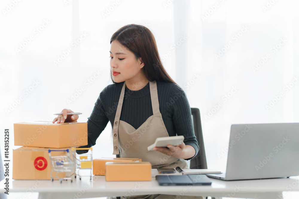 Online Business Owner Managing Orders: A focused young Asian woman, wearing an apron, meticulously manages orders at her home office, surrounded by shipping boxes, a calculator, and laptop. Online Business Owner Managing Orders: A focused young Asian woman, wearing an apron, meticulously manages orders at her home office, surrounded by shipping boxes, a calculator, and laptop.