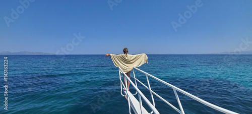 a beautiful girl stands on the prow of a pleasure yacht and spread her arms to the sides. the child enjoys the warm sun and fresh sea breeze. travel and summer holiday destination