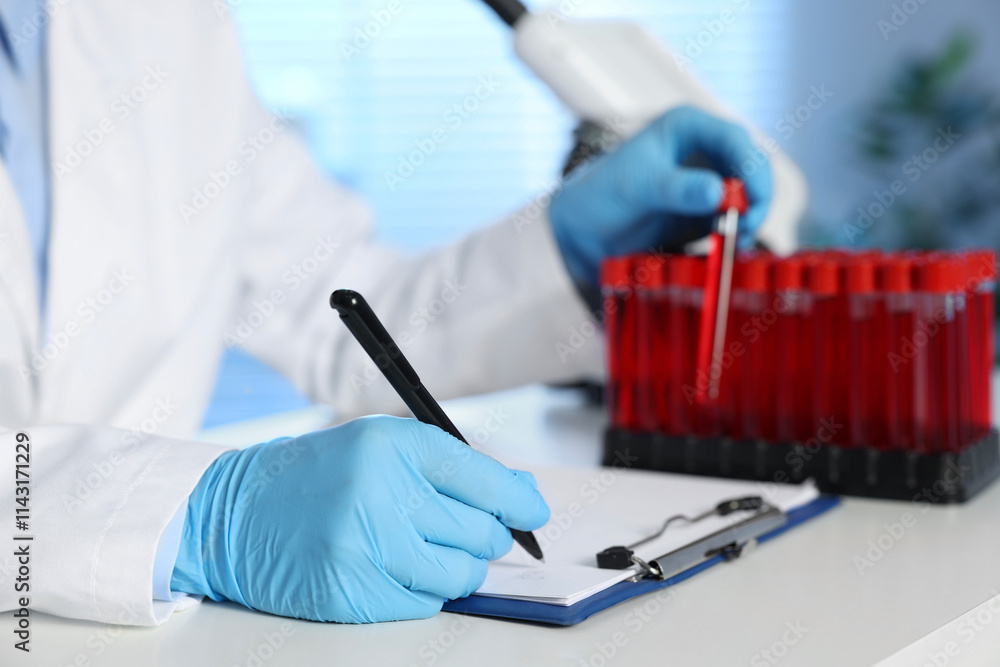 Laboratory testing. Doctor taking test tube with blood sample while working at table indoors, closeup Laboratory testing. Doctor taking test tube with blood sample while working at table indoors, closeup