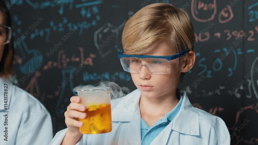 Closeup of smart boy inspect mixed chemical liquid in laboratory beakers while holding and looking carefully. Child focus on doing an experiment in chemistry lesson or STEM science class. Erudition. Closeup of smart boy inspect mixed chemical liquid in laboratory beakers while holding and looking carefully. Child focus on doing an experiment in chemistry lesson or STEM science class. Erudition.