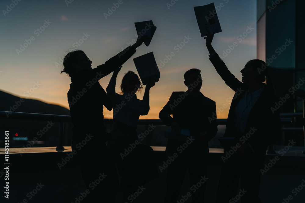 Obraz premium Silhouetted business people raising documents and celebrating success against a picturesque sunset. The group is outdoors, showcasing teamwork, achievement, and triumph in a professional setting.