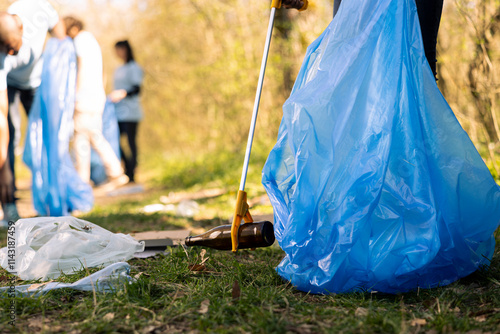 Volunteers group gathering to tidy up the woods of garbage, fighting forest pollution to protect the natural ecosystem. Team of activists collecting rubbish and plastic waste with tools.
