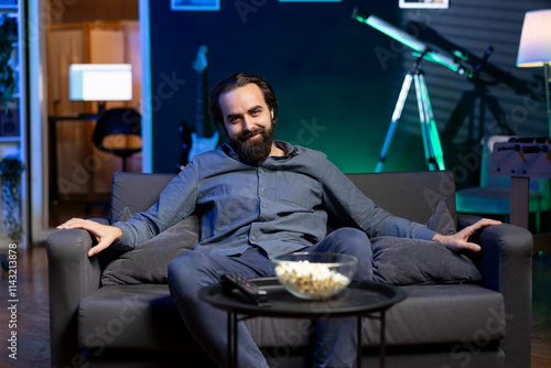 Portrait of happy person using TV to binge series on subscription based streaming services, enjoying bowl of popcorn. Joyful man relaxing at home watching VOD shows on television display, eating snack photo