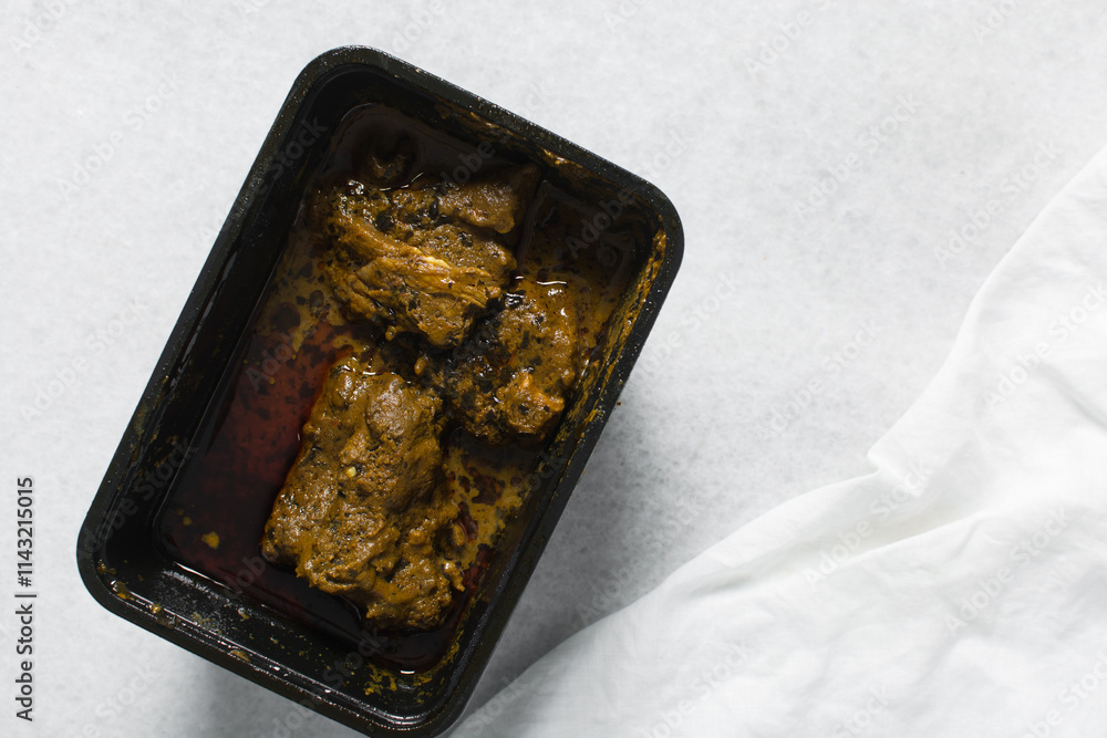 Overhead view of Nigerian banga soup with fish and beef in a plastic container, top view of palm nut soup in a takeaway plate, traditional palm nut soup in a black plate Overhead view of Nigerian banga soup with fish and beef in a plastic container, top view of palm nut soup in a takeaway plate, traditional palm nut soup in a black plate