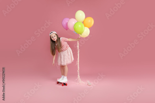 Little girl with colorful balloons standing on penny board against pink background